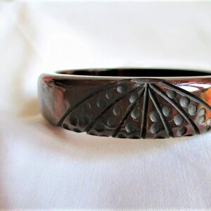 May include: A dark brown, carved, plastic bangle bracelet with a geometric pattern.