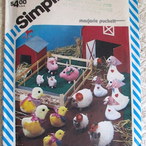 May include: A Simplicity 6353 sewing pattern envelope featuring illustrations of stuffed farm animals including pigs in a fenced pen, yellow chicks with purple ribbons, white sheep with red flower accents, and white geese wearing patterned bonnets.