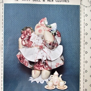May include: A 12-inch fabric doll dressed in a pink and white floral dress with a white lace apron. The doll is sitting on a chair with a teacup and teapot on a table in front of her. The image is from a pattern for a doll and her clothes.
