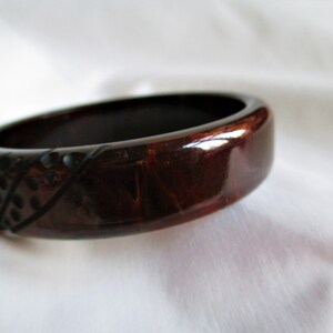 May include: A dark brown and black bangle bracelet with a geometric pattern. The bracelet is made of a shiny material and has a smooth finish.