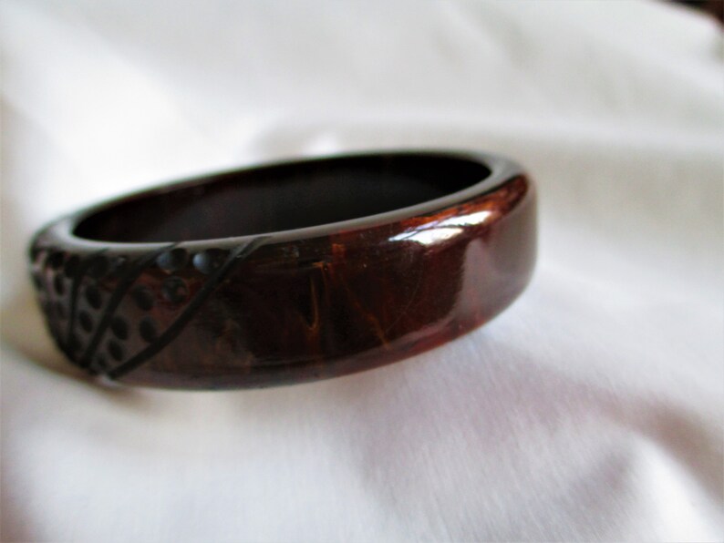 May include: A dark brown and black bangle bracelet with a geometric pattern. The bracelet is made of a shiny material and has a smooth finish.