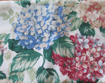 May include: A white fabric with a floral pattern featuring blue, pink, and white hydrangeas. The fabric has a textured, linen-like appearance.