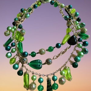 May include: A layered necklace with a mix of green beads and pendants. The necklace showcases various green beads and pendants, including round, oblong, and teardrop shapes, in emerald, lime, and forest green, on gold-tone chains.