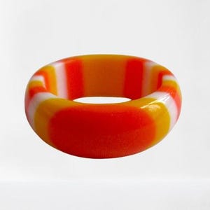 Puede incluir: Un anillo colorido con un diseño a rayas. El anillo presenta una combinación de rayas rojas, naranjas, amarillas y blancas. El anillo es un accesorio llamativo, perfecto para añadir un toque de color a cualquier atuendo.