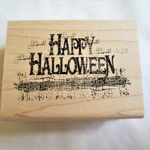 Puede incluir: Un sello de goma rectangular de madera con el texto negro Happy Halloween en una fuente de estilo gótico desgastado. El sello tiene un acabado de madera de color tostado claro con veta y el diseño está centrado en la cara frontal.