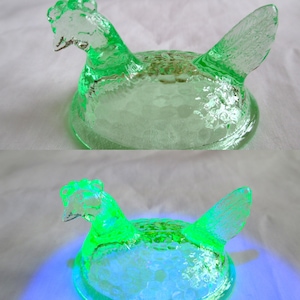 Puede incluir: Un plato de vidrio verde con forma de gallina y superficie texturizada. La gallina tiene una cresta, pico y alas detallados. El plato está diseñado para guardar objetos pequeños y probablemente sea vintage o antiguo.