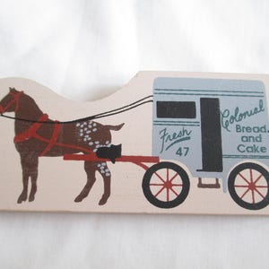 Può includere: Una sagoma piatta in legno raffigurante un cavallo marrone con macchie bianche che traina un carro da consegna azzurro. Il carro ha ruote nere con raggi rossi e la scritta Fresh 47 e Colonial Bread and Cake in caratteri neri e blu.
