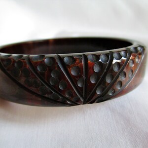 May include: A dark brown plastic bangle bracelet with a carved design of black circles and lines.