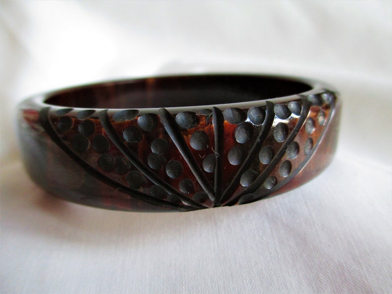 May include: A dark brown plastic bangle bracelet with a carved design of black circles and lines.