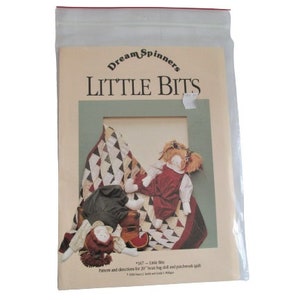 Può includere: Un opuscolo di modelli e istruzioni per una bambola di pezza da 50 cm e una trapunta patchwork. La copertina presenta una trapunta patchwork colorata con due bambole sedute sopra. Il titolo dell'opuscolo è "Dream Spinners Little Bits".