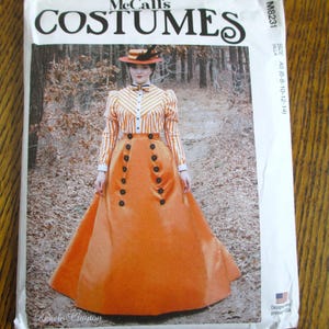 Könnte beinhalten: McCall's Costumes Schnittmusterpackung mit einem Vintage-Kleid in Orange und Weiß gestreift mit schwarzen Knöpfen und passendem Hut. Das Paket enthält den Text "McCall's Costumes" und "M8231". Das Design stammt von Angela Clayton.