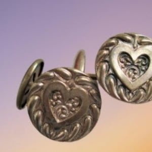 May include: Two silver cufflinks with a heart design. The hearts are detailed with intricate swirls and are surrounded by a textured border.