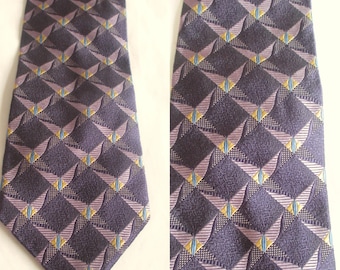 Può includere: Una cravatta con base viola scuro e un motivo geometrico ripetuto di accenti a forma di diamante in viola chiaro, giallo e blu. Il tessuto ha un aspetto testurizzato con un'estremità appuntita e un design a lama larga.