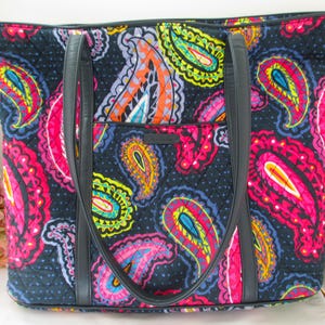 Puede incluir: Bolso tote grande con un colorido estampado de cachemir en tonos rosa, naranja, amarillo y azul sobre un fondo azul marino. El bolso tiene asas negras y un bolsillo frontal. El bolso mide aproximadamente 46 cm de ancho y 30 cm de alto.