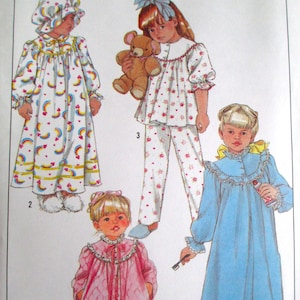 May include: Simplicity pattern featuring children's sleepwear designs. The designs include a long white nightgown with rainbow and heart patterns, a pink nightgown, a blue nightgown, and a floral pajama set. The pattern includes the Simplicity logo.