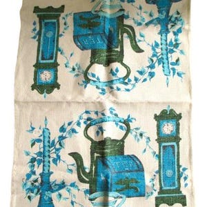 May include: A beige tea towel with a repeating pattern of teal and green teapots, clocks, and floral vines. The word "TEA" is visible on the teapot. The design has a vintage aesthetic.