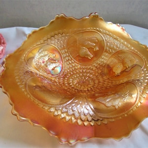 Peut inclure: Un grand bol en verre ambré iridescent avec un bord festonné. Le bol présente un motif en relief de quatre têtes d'animaux dans des médaillons.