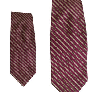 May include: A burgundy tie with thin, diagonal stripes in a light beige color. The tie is made of a smooth fabric and is displayed against a white background. The tie is a classic accessory for formal or business attire.