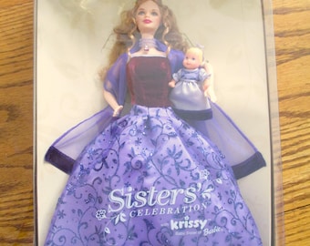 May include: Barbie Sisters' Celebration doll set featuring a purple gown with a floral pattern and a matching baby doll. The box features the text "Sisters' Celebration with Krissy Baby Sister of Barbie".