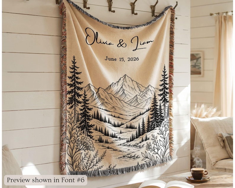 Personalized mountain woven blanket with custom couple names and date, featuring forest trees and rustic mountain landscape art, styled as cozy cabin wall decor for wedding, engagement, or anniversary gift.