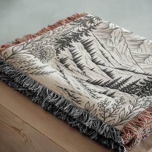Personalized mountain woven blanket with custom couple names and date, featuring forest trees and rustic mountain landscape art, styled as cozy cabin wall decor for wedding, engagement, or anniversary gift.