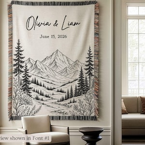 Personalized mountain woven blanket with custom couple names and date, featuring forest trees and rustic mountain landscape art, styled as cozy cabin wall decor for wedding, engagement, or anniversary gift.
