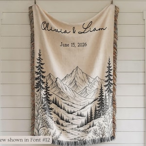 Personalized mountain woven blanket with custom couple names and date, featuring forest trees and rustic mountain landscape art, styled as cozy cabin wall decor for wedding, engagement, or anniversary gift.