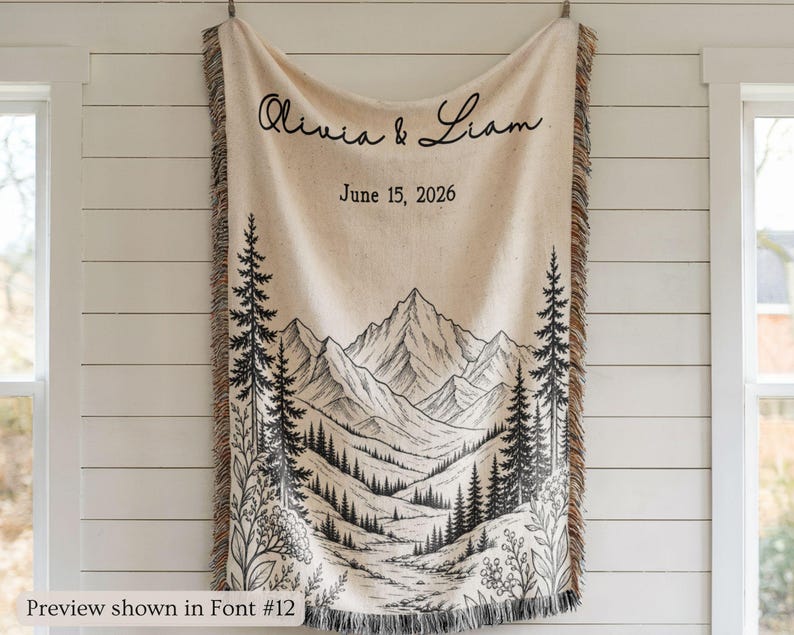Personalized mountain woven blanket with custom couple names and date, featuring forest trees and rustic mountain landscape art, styled as cozy cabin wall decor for wedding, engagement, or anniversary gift.