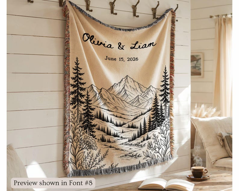 Personalized mountain woven blanket with custom couple names and date, featuring forest trees and rustic mountain landscape art, styled as cozy cabin wall decor for wedding, engagement, or anniversary gift.