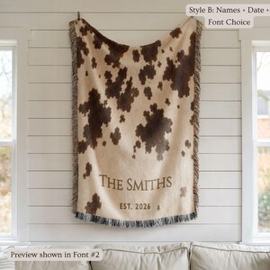 Personalized cow print woven blanket with custom couple names and wedding date, brown and cream western pattern, rustic farmhouse wall decor, fringe edges, and cozy country wedding keepsake style.