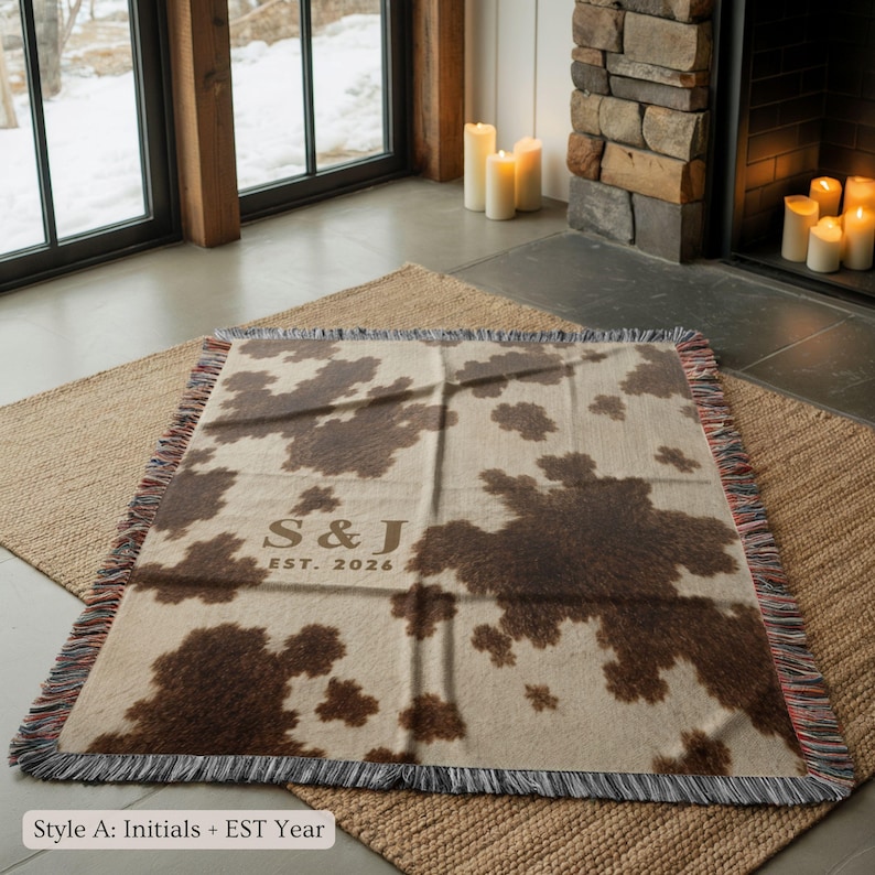 Personalized cow print woven blanket with custom initials and established year, brown and cream western pattern, rustic farmhouse wall decor, fringe edges, and cozy country couple keepsake style.