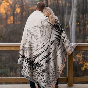 Personalized mountain woven blanket with custom couple names and date, featuring forest trees and rustic mountain landscape art, styled as cozy cabin wall decor for wedding, engagement, or anniversary gift.