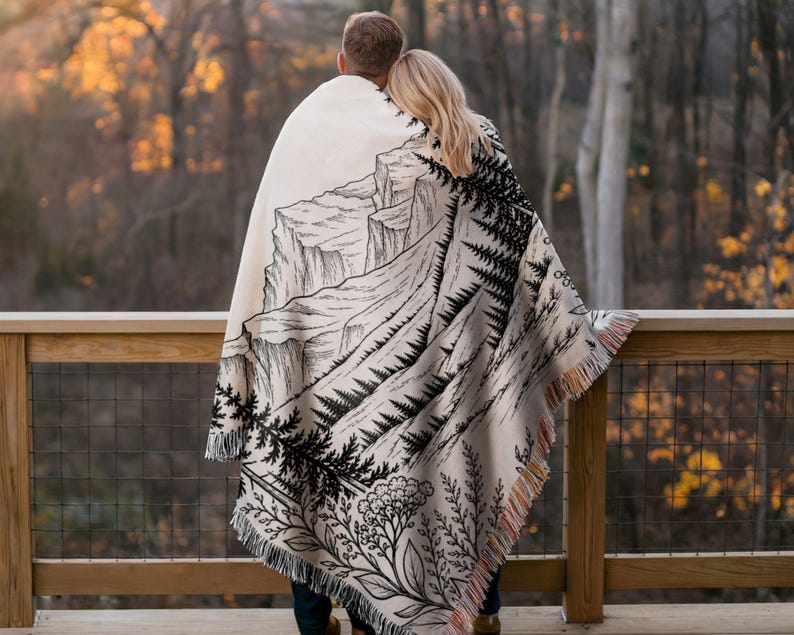 Personalized mountain woven blanket with custom couple names and date, featuring forest trees and rustic mountain landscape art, styled as cozy cabin wall decor for wedding, engagement, or anniversary gift.
