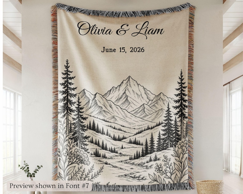 Personalized mountain woven blanket with custom couple names and date, featuring forest trees and rustic mountain landscape art, styled as cozy cabin wall decor for wedding, engagement, or anniversary gift.
