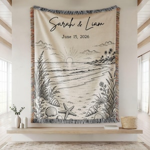 May include: A woven beach-themed tapestry with a black and white illustration of a sunset over the ocean, seashells, and beach grass. The names "Sarah & Liam" and the date "June 15, 2026" are written in script.