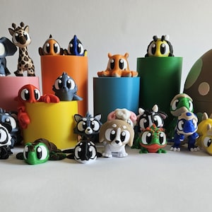 Könnte beinhalten: Eine Sammlung farbenfroher Cartoon-Tierfiguren, darunter ein Elefant, eine Giraffe, ein Oktopus, eine Biene und eine Schildkröte. Die Figuren sind auf und um zylindrische Ständer in verschiedenen Farben angeordnet, mit einem großen pilzförmigen Behälter im Hintergrund.