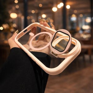 May include: A light pink phone case with a clear back and a matching ring holder. The case has a square camera protector with the text "CASE PRO". The ring holder is attached to the case with a hinge.