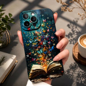 May include: A teal phone case with a colourful illustration of an open book and butterflies. The design shows butterflies emerging from the pages against a dark blue background. The case has a whimsical and artistic aesthetic.