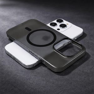 May include: A dark gray phone case with a black circular magnetic charging area. The case is resting on a white phone with a silver frame and three camera lenses. The background is a dark gray surface.