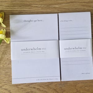May include: Two white notepads with the text "thoughts go here..." and "a few things to do..." are displayed. The notepad is wrapped with a band that reads "underwhelm me". Yellow daffodils are on the left.