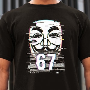 May include: Black t-shirt with a white mask design, glitch effects, and the number 67 in white. The mask has a stylized face with closed eyes and a smile. The shirt is made of a soft material.