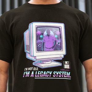 May include: Black t-shirt featuring a retro computer graphic with a person inside the screen, palm trees, and the text "I'M NOT OLD, I'M A LEGACY SYSTEM." A floppy disk icon is also present. The design has a vaporwave aesthetic.