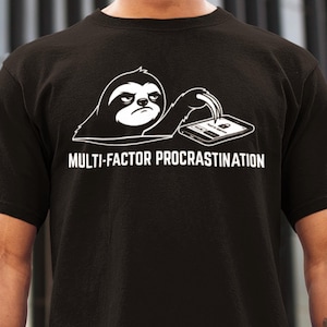 Op de afbeelding: Zwart t-shirt met een witte afbeelding van een luiaard die naar een smartphone kijkt. De tekst "MULTI-FACTOR PROCRASTINATION" staat eronder. Een casual kledingstuk.