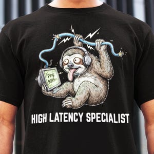 May include: Black t-shirt featuring a cartoon sloth wearing headphones and holding a computer displaying a high ping. The sloth is holding a damaged blue cable. The text "HIGH LATENCY SPECIALIST" is printed below the graphic.