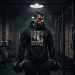 May include: Black hoodie with a graphic design featuring the text "HAUNTED BY UNDOCUMENTED CODE" and Japanese text. The design includes an illustration of a ghost and a computer. The person is holding two dumbbells.