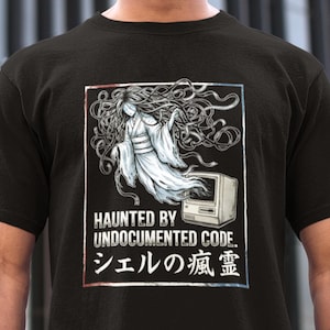 May include: Black t-shirt with a graphic of a spectral figure and a retro computer. The text reads "HAUNTED BY UNDOCUMENTED CODE." and Japanese characters. The design is framed in red and blue.
