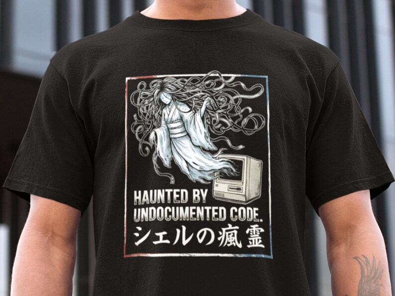 May include: Black t-shirt featuring a graphic of a ghostly figure with long flowing hair and a vintage computer. The text reads "HAUNTED BY UNDOCUMENTED CODE." and Japanese characters. The design is framed in red and blue.