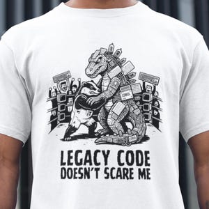 May include: White t-shirt featuring a black and white graphic of a Godzilla-like creature wrestling a badger. The text "LEGACY CODE DOESN'T SCARE ME" is printed below the graphic.