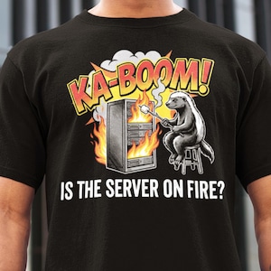Op de afbeelding: Zwart T-shirt met een humoristische afbeelding. Het ontwerp toont een server in brand, een das die een marshmallow roostert, en de tekst "KA-BOOM! IS THE SERVER ON FIRE?" in geel en rood.
