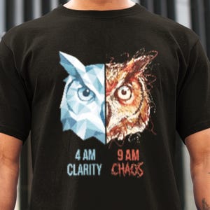 Op de afbeelding: Zwart t-shirt met een gesplitst uil-ontwerp. De ene helft is een geometrische blauwe uil, de andere een gedetailleerde bruine uil. De tekst hieronder luidt "4 AM CLARITY" en "9 AM CHAOS".
